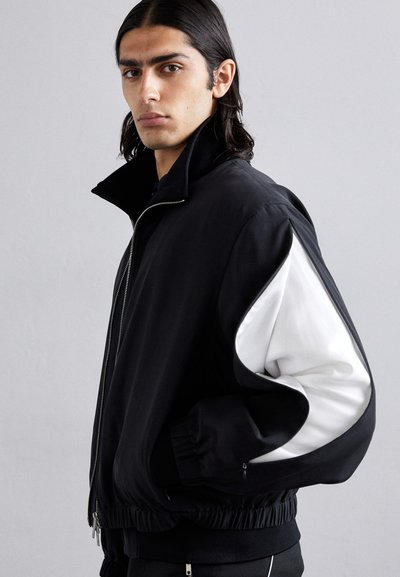 Schwarze Bomberjacke mit hohem Kragen, featuring weiße Akzentpaneele an den Ärmeln, Reißverschluss, elastischen Bündchen und Saum. Glatte Stofftextur.