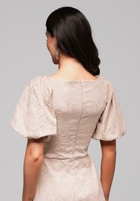 Robe à manches bouffantes en tissu beige clair avec une texture florale, dotée d'un décolleté carré et d'une fermeture éclair au dos.