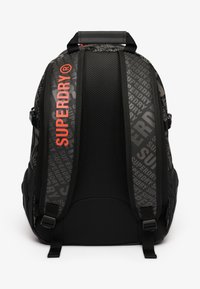 Czarny plecak z siateczkowym tyłem, z logo "SUPERDRY" w kolorze czerwonym oraz powtarzającym się szarym wzorem. W zestawie regulowane szelki i uchwyt górny.