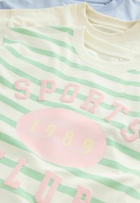 Trzy koszulki T-shirt w poziome zielono-białe paski, z różowym napisem "SPORTS CLUB" oraz rokiem "1989" w kolorze żółtym.