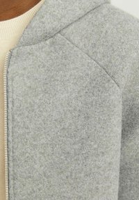 Grau gefütterte Jacke mit Kapuze, die eine weiche Textur, einen kontrastierenden Reißverschluss und ein strukturiertes Design aufweist. Nahaufnahme des Schulterbereichs.