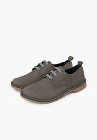 Scarpe in suede grigio con una texture liscia, dotate di lacci grigi e una suola in gomma marrone. Punta arrotondata e linguetta posteriore per una facile calzata.