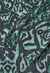 Tissu à motif abstrait dans des teintes de vert et de noir. Présente une texture lisse avec des designs tourbillonnants et un bord plié.