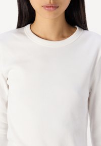 Top lungo a maniche ribbed bianche con scollatura rotonda e una consistenza morbida, incentrato su una silhouette aderente senza cuciture visibili.