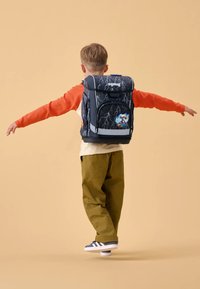 Sac à dos noir et gris avec motif d'éclair et graphique animal coloré, doté de bretelles ajustables et d'une poignée supérieure, porté par un enfant.