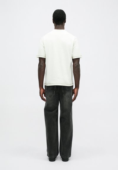 Camiseta de algodón gris claro con mangas cortas, combinada con jeans de pierna ancha gris oscuro. El conjunto tiene un corte holgado y un diseño minimalista.