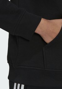 Svart sweatshirt med ribbade muddar, en känguruficka och strukturerad tyg. Har en enfärgad design utan mönster eller dekorationer.