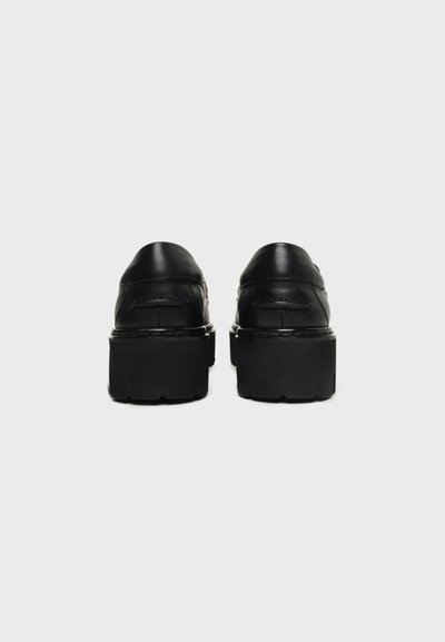 Paire de chaussures à plateforme en cuir noir avec semelles épaisses vues de dos sur fond blanc uni.