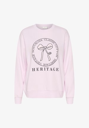Lyserød sweatshirt med sort omrids af sløjfe og tekst, der læser "Classic Cotton Heritage Vintage Nostalgia" i en cirkel, og "HERITAGE" nedenunder.