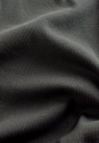 Primer plano de tela acanalada gris oscuro con pliegues suaves y sombras que resaltan su textura y patrón de tejido.