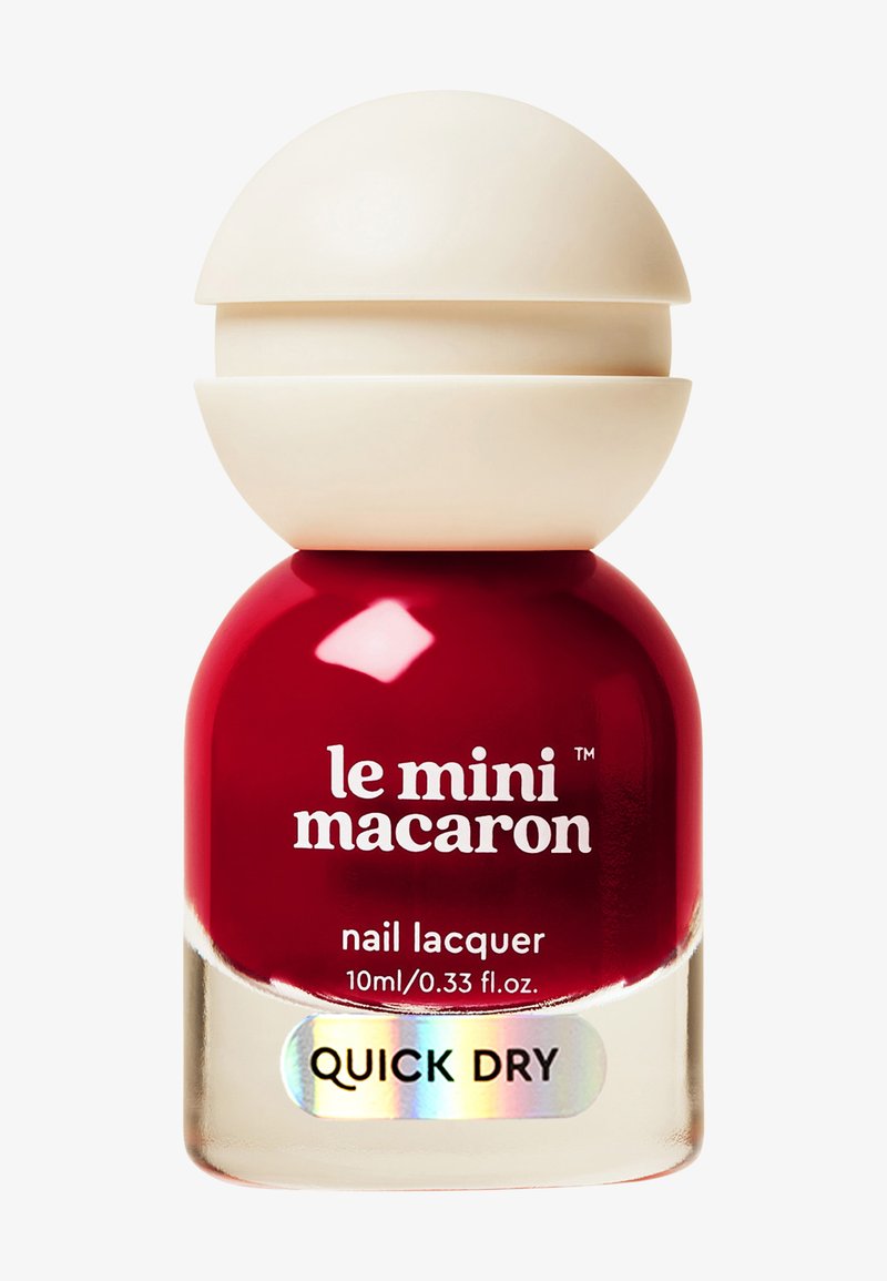 Flesje rode nagellak met het label "le mini macaron", een afgeronde beige dop en een sticker met "quick dry" op een witte achtergrond.