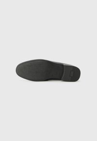 Suela de zapato de cuero negro con un acabado liso, que presenta una forma curvada, agarre texturizado y una costura visible a lo largo de los bordes.