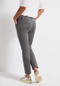 Pantalons gris slim-fit en tissu lisse, dotés de poches arrière et d'une taille mi-haute, associés à des baskets décontractées.