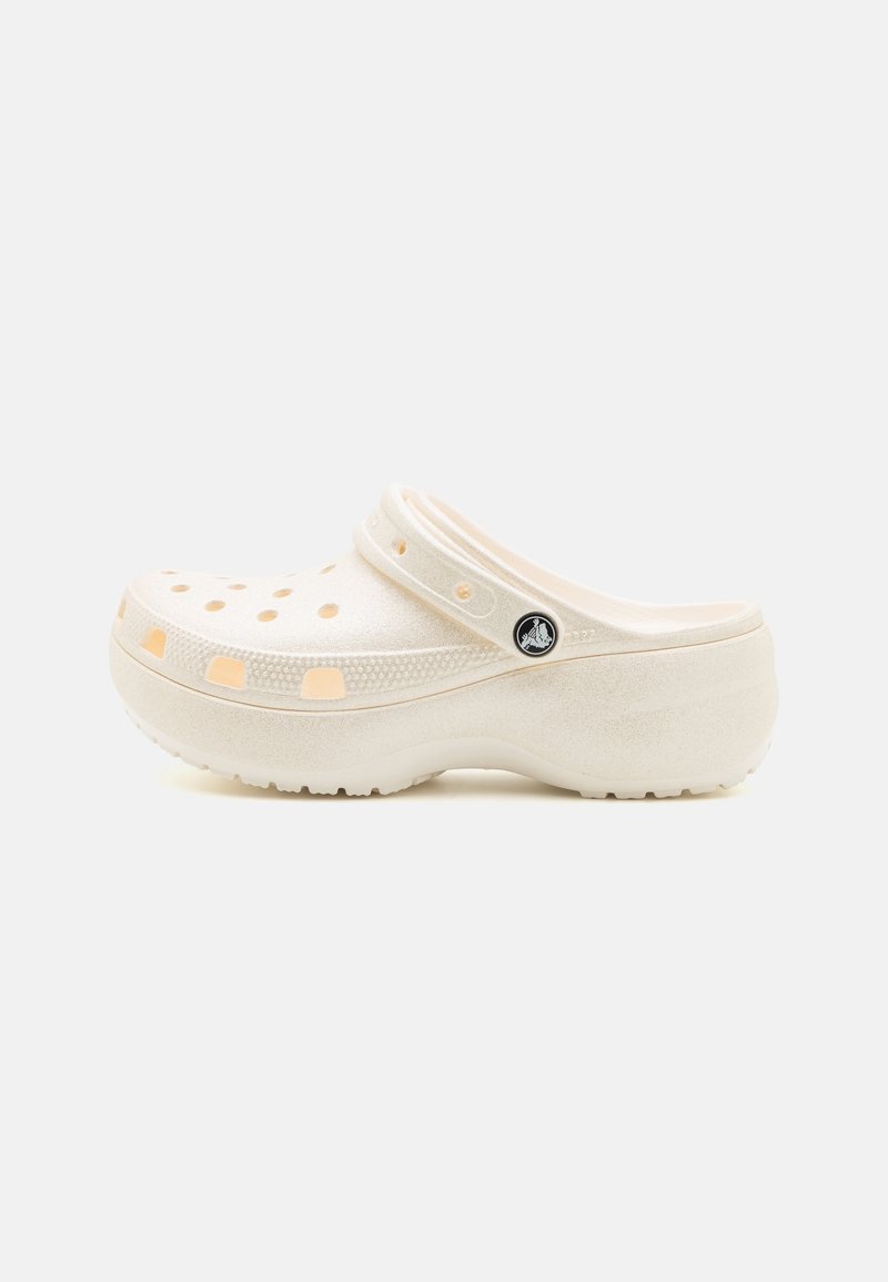 Sabot beige à enfiler avec des trous de ventilation, une bride de talon ajustable, une semelle texturée et un logo rond de la marque sur le côté.