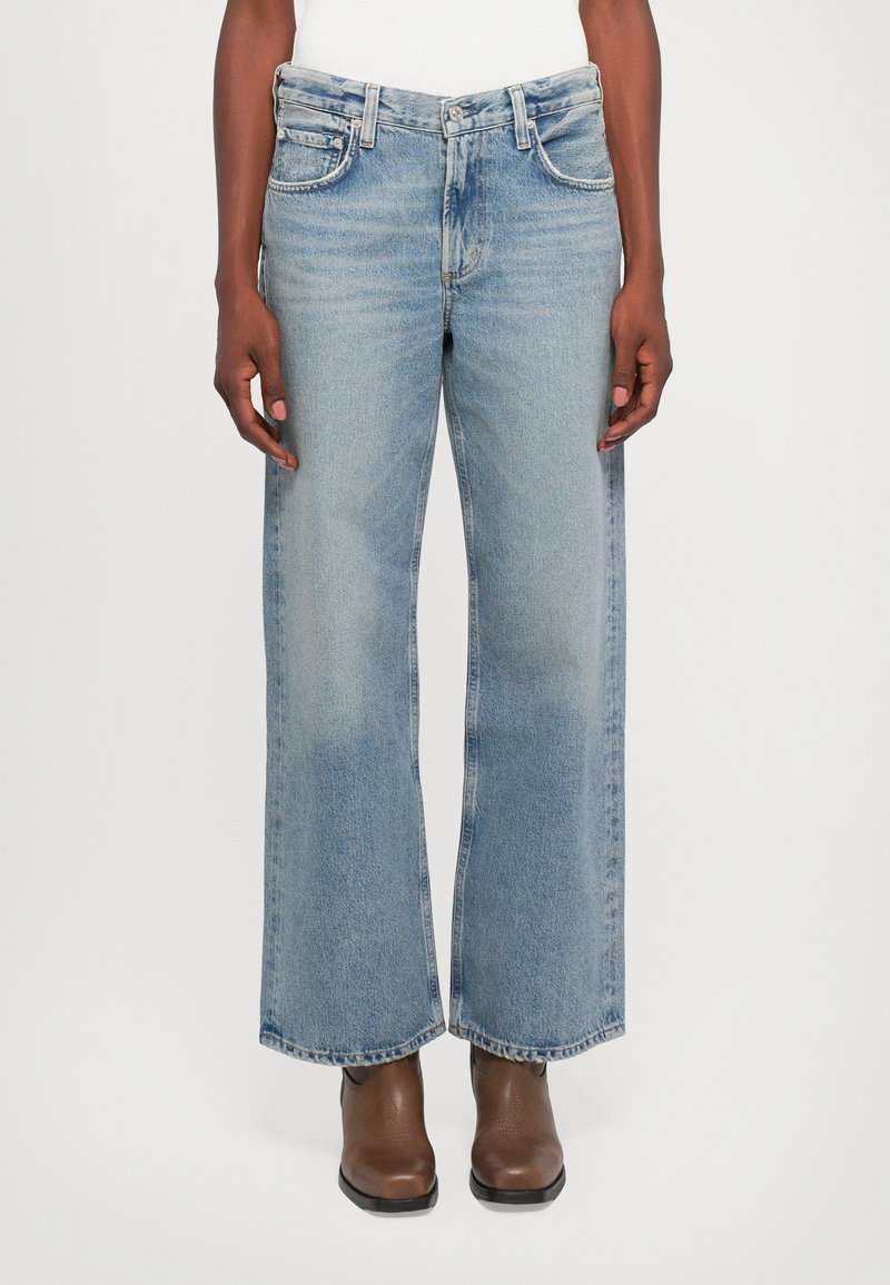Light blue wide-leg jeans in a faded denim material. Features five pockets and a classic button and zipper fly. Worn with brown boots.