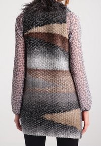 Cardigan lungo realizzato in un tessuto a maglia testurizzato; presenta un motivo a gradiente in grigio, marrone e crema, con un colletto in pelliccia sintetica e maniche trasparenti.