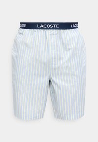 Boxer bleu clair avec des rayures verticales jaunes et blanches, taille élastique bleu marine avec "LACOSTE" en lettres blanches.
