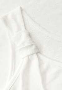 Tissu blanc au toucher lisse, avec un détail froncé à l'épaule. Le design comprend une encolure large et des coutures douces.
