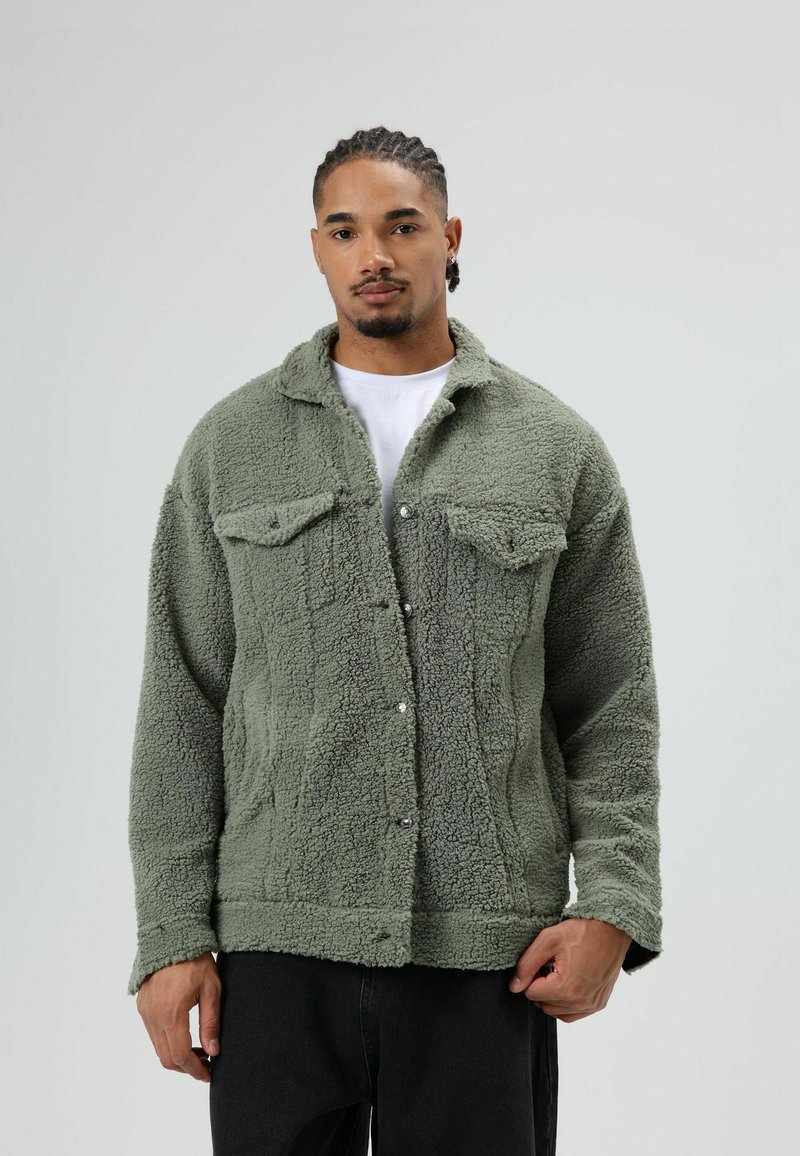 Fuzzy olive green fleece jacket with snap buttons, side pockets, and chest pockets. Features a shearling texture and a collared neckline.