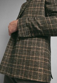 Blazer a quadri marrone realizzato in tessuto testurizzato, con due bottoni ai polsini e una vestibilità su misura.