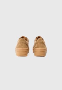 Tan suede sneakers with a textured fur accent at the back, featuring a chunky, light brown rubber sole and stitched detailing.