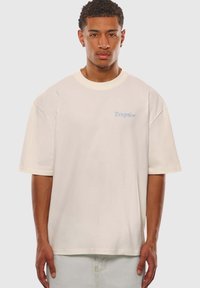 Beige oversized T-shirt med rund halsudskæring og korte ærmer. På fronten til venstre er der lysblå tekst med "Dropsize". Blødt bomuldsmateriale.