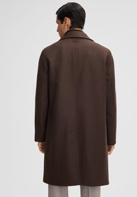 Bruine wollen overjas met een op maat gemaakte uitstraling, reverskraag en enkele split. Bevat een zichtbare naaddetails aan de achterkant.