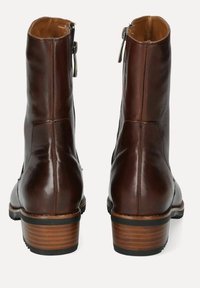 Botas de cuero marrón hasta el tobillo con un acabado liso, cremallera trasera y un tacón de madera apilada. Presenta costuras mínimas y una punta redondeada.
