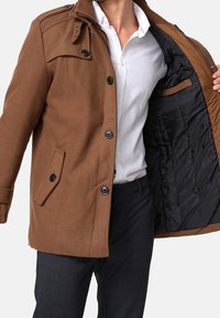 Bruine jas van een wolmix met knoopsluiting en zijzakken, uitgevoerd met een doorgestikte zwarte binnenvoering en een contrasterende kraag.