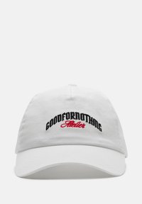 Witte katoenen pet met zwart en rood geborduurde tekst "GOODFORNOTHING Atelier" op de voorkant. Klassiek ontwerp met een gebogen rand.