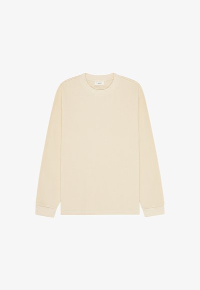 Chemise beige à manches longues en maille gaufrée avec col rond et poignets côtelés, posée à plat sur un fond blanc.