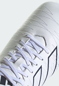Zapato de fútbol de cuero blanco con costuras en zigzag, cordones blancos planos y un diseño de acento azul. Textura suave con punta redondeada.