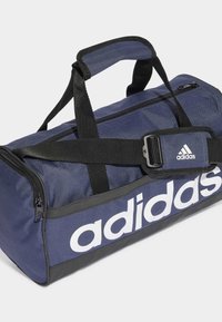 Borsa a tracolla blu navy realizzata in tessuto resistente, con un grande logo bianco, cinturini neri e un compartimento principale con zip.