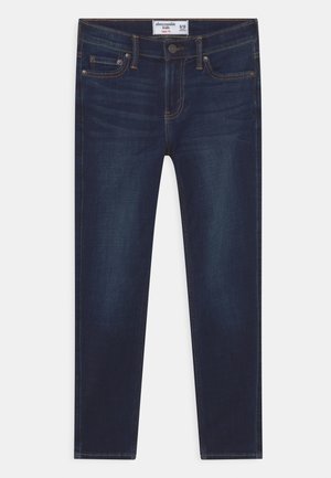 Jean en denim bleu foncé avec une coupe fuselée, design à cinq poches, et accents en laiton. Présente une texture lisse et de poids moyen.