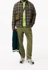 Rutigt skjorta med svarta och bruna rutor, lager på en grön ribbad tröja. Olivgröna kordbyxor, grå-svarta sneakers och en grön stickad cardigan.