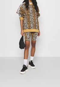 Oversized sweatshirt i leopardmönster med gula detaljer samt matchande cykelbyxor i leopardmönster. Svarta sneakers och en liten svart väska fulländar looken.