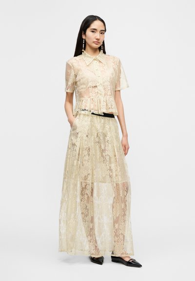 Σετ από δύο κομμάτια δαντέλα που περιλαμβάνει πουκάμισο με κοντά μανίκια και μακριά φούστα. Χρώμα: απαλό μπεζ. Διαφανής υφή με λουλουδένια σχέδια. Μαύρη ζώνη ως διακοσμητικό στοιχείο.