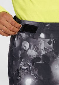 Černé a šedé vzorované kalhoty s uzavíráním v pase na suchý zip; mají šikmou kapsu s táhlem a strukturovaný povrch.