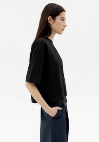 Schwarzes Baumwoll-T-Shirt mit kurzen Ärmeln, Rundhalsausschnitt, cropped Design und einer glatten Textur, getragen zu dunklen Hosen.