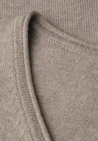 Tejido de punto beige con una superficie texturizada y bordes acanalados. El material parece suave, con una sección doblada y un grano sutil.