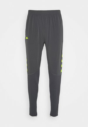 Donkergrijze sportbroek met elastische taille, taps toelopende pijpen, neongele logo's aan de zijkanten en knie-naaddetails.