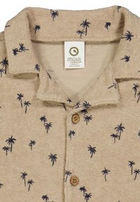 Vaaleanbeige paita, jossa on kaulus ja pieniä tummansinisellä palmupuulla varustettuja kuvioita. Kiinnitetty kahdella puunappi. Tagi lukee "müsli."