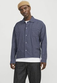 Marineblå og hvid ternet skjorte med krave, lange ærmer og frontknapper; parret med mørke denimbukser.