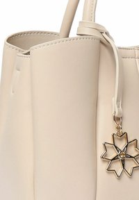 Beige leren totebag met gestructureerd ontwerp en een gladde textuur. Voorzien van een gouden stervormige bedel die aan een band is bevestigd.