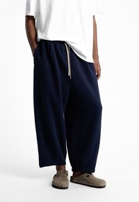 Pantalons large bleu marine avec un cordon de serrage à la taille, associés à un t-shirt blanc. Le matériau semble doux ; les pantalons ont une coupe décontractée.