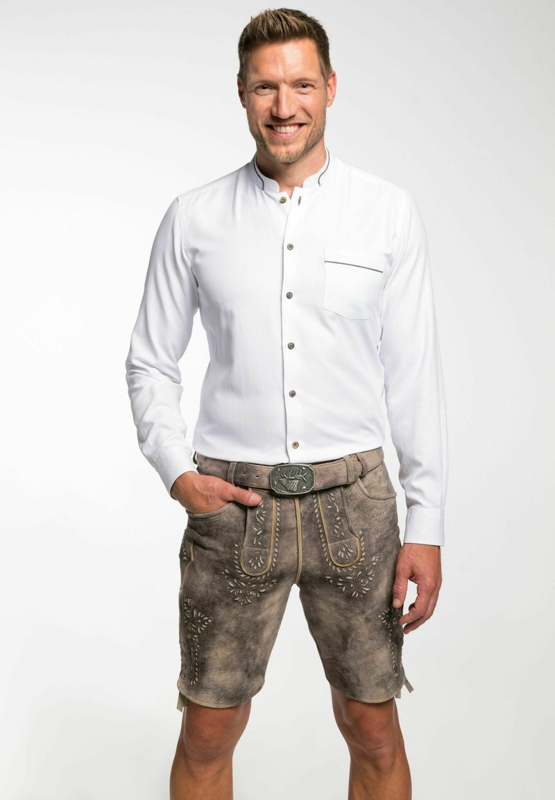 Weißes Langarmhemd mit Knopfdetails, kombiniert mit grauen Lederhosen mit dekorativer Stickerei und einem Gürtel mit einer metallischen Schnalle.