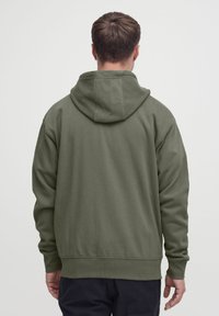 Roheline kapuutsiga pusa, valmistatud pehmest materjalist. Sellel on kengurutasku, soonilised varrukasuusad ja alläär. Klassikalise lõikega, tagakülg on ühtlane.