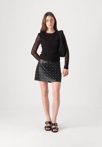 Svart langermet topp med røde prikkene, kombinert med en svart skinn mini skjørt med sølvstudder. Modellen har en teksturert svart skulderveske.