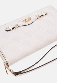 Portefeuille texturé blanc avec quincaillerie dorée, logo embossé et accents noirs. Comprend une fermeture éclair et une sangle pour poignet pour un transport sécurisé.