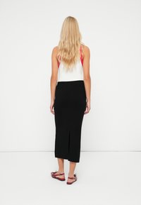Jupe midi noire avec une fente arrière, faite d'un matériau lisse. Associée à un haut sans manches blanc et rouge et des ballerines rouges.